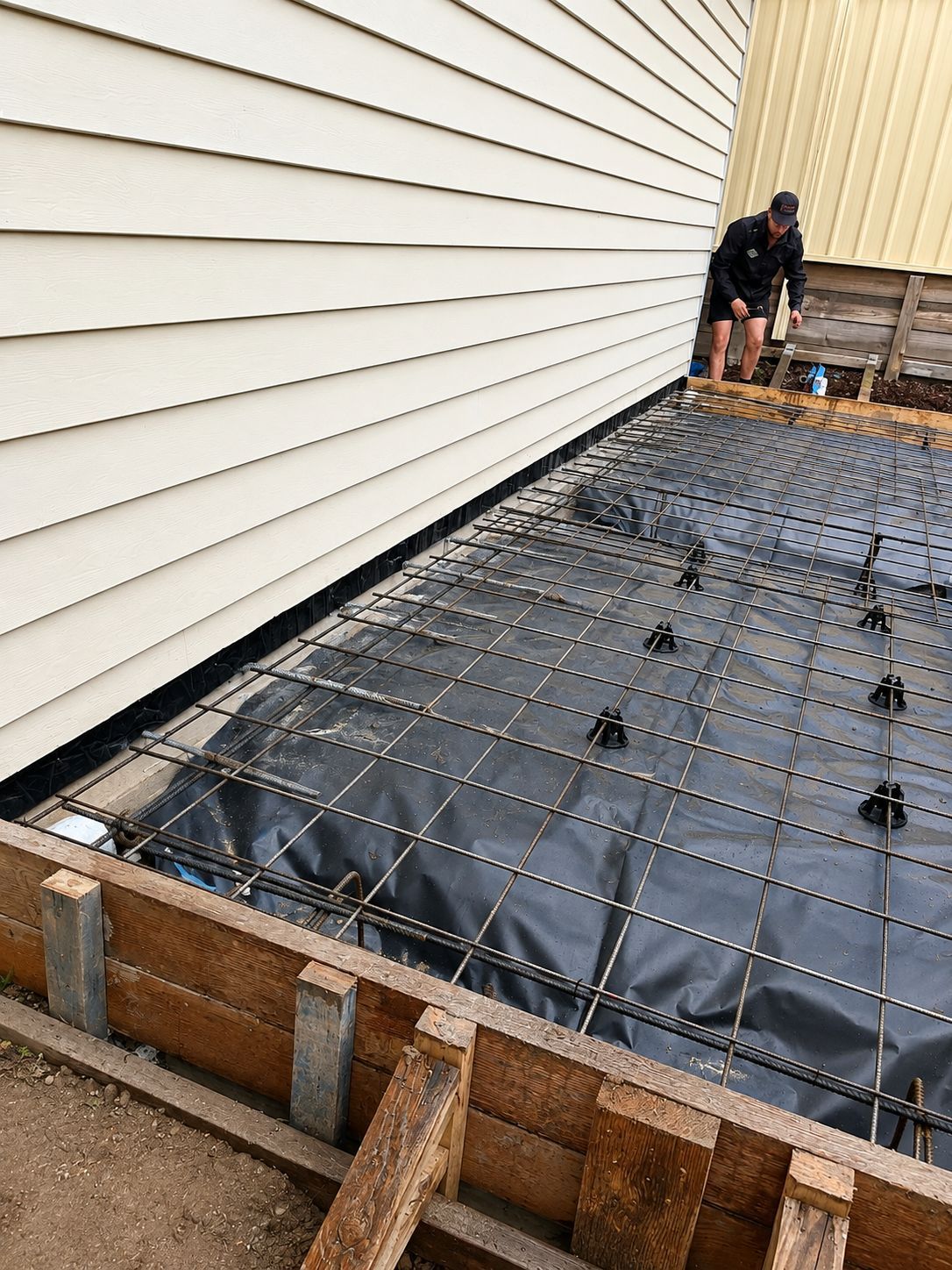 Technician laying the barrier membrane and reinforcement mesh beside a house before the pour